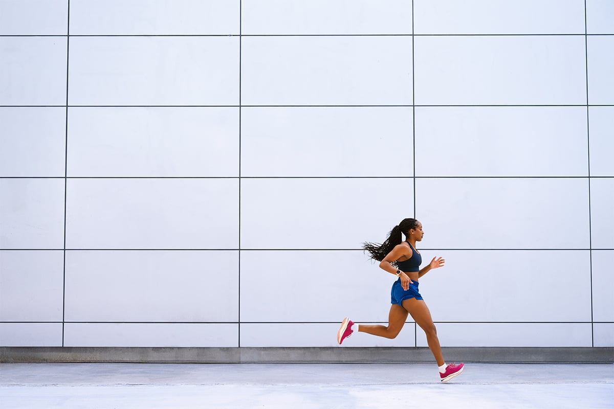 Một người phụ nữ đeo smartwatch Garmin Forerunner 970 đang chạy bộ trước một tòa nhà.